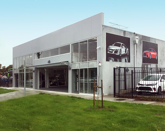 A modern building, the Audi service centre, with grand entrance and cars in the yard.